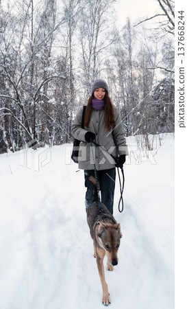 A young woman relaxes during a walk in a winter forest with her dog. A young woman relaxes during a walk in a winter forest with her dog. 137668244