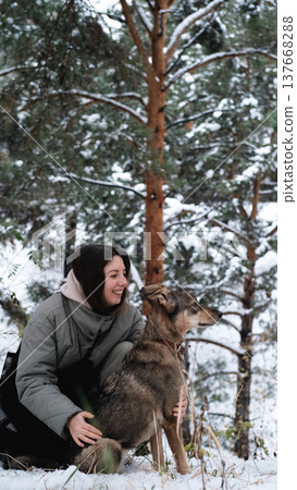 A young woman walks through a winter pine forest with her dog A young woman walks through a winter pine forest with her dog 137668288