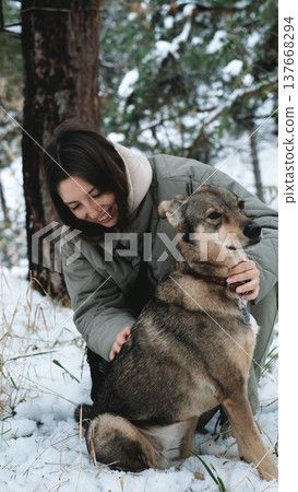 A young woman walks through a winter pine forest with her dog A young woman walks through a winter pine forest with her dog 137668294