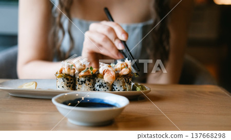 A beautiful girl eats Japanese sushi rolls with chopsticks, smiling with pleasure A beautiful girl eats Japanese sushi rolls with chopsticks, smiling with pleasure 137668298