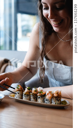 A beautiful girl eats Japanese sushi rolls with chopsticks, smiling with pleasure A beautiful girl eats Japanese sushi rolls with chopsticks, smiling with pleasure 137668299
