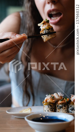 A beautiful girl eats Japanese sushi rolls with chopsticks, smiling with pleasure 137668312