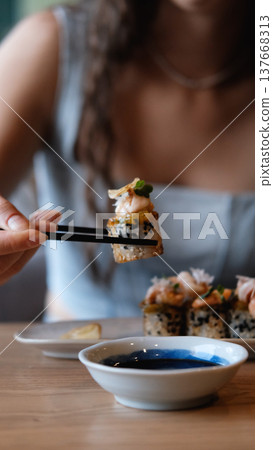 A beautiful girl eats Japanese sushi rolls with chopsticks, smiling with pleasure A beautiful girl eats Japanese sushi rolls with chopsticks, smiling with pleasure 137668313