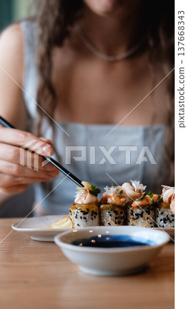 A beautiful girl eats Japanese sushi rolls with chopsticks, smiling with pleasure 137668343