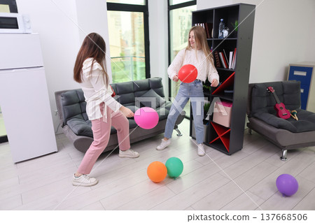 Two friends enjoy a lively moment playing with colorful balloons indoors in a bright and cheerful setting 137668506