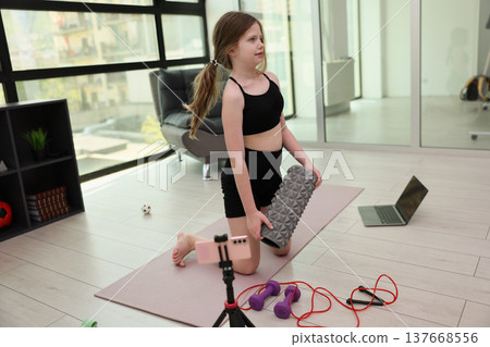 Young girl practices yoga and fitness at home with colorful equipment on a sunny day Young girl practices yoga and fitness at home with colorful equipment on a sunny day 137668556