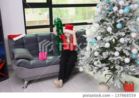 Cheerful girl celebrates the holidays with festive decorations and gifts in a cozy living room setting 137668559