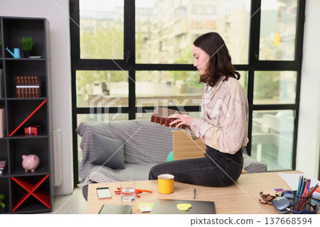 Reading a treasured book while sitting at a cozy desk in a modern sunlit apartment filled with greenery and inspiring decor 137668594