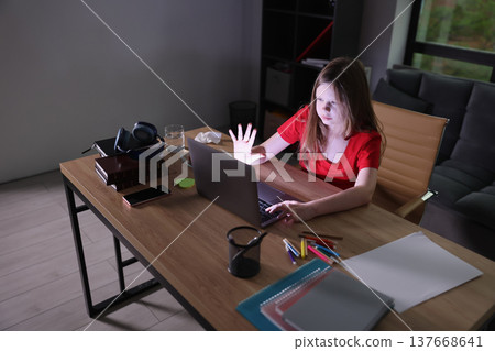 Focused girl working on a laptop in a cozy room with evening shadows highlighting her creativity and determination 137668641