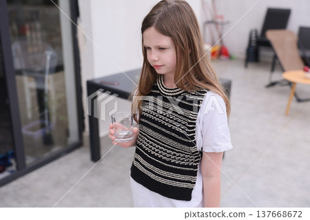 Young girl in a cozy knitted sweater holding a glass in a modern indoor space during a quiet afternoon Young girl in a cozy knitted sweater holding a glass in a modern indoor space during a quiet afternoon 137668672