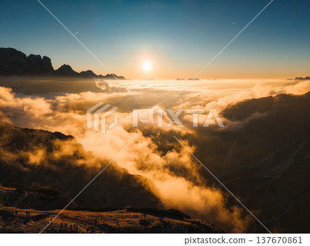 Golden sunrise shines over sea of fog over rugged alpine mountain ridge in Dolomites, Italy 137670861