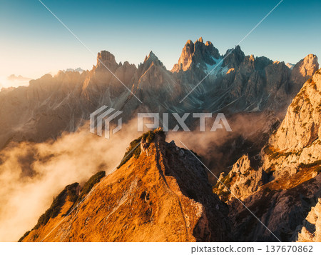 Scenic view of golden sunrise over rugged steep peaks of Cadini di Misurina with rising fog in Dolomites, Italy 137670862