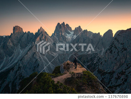 Alpine landscape of Cadini di Misurina with rugged mountain peak and male tourist hiking during sunset in Dolomites, Italy 137670898