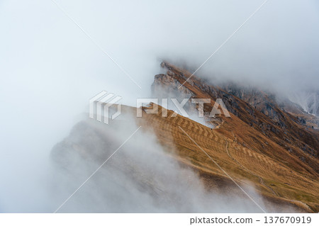 Foggy mountain ridge with hiking trail and rugged alpine landscape in Seceda, Dolomites Foggy mountain ridge with hiking trail and rugged alpine landscape in Seceda, Dolomites 137670919