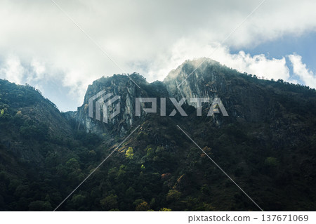 Mountain cliff above dense forest under dramatic sky Mountain cliff above dense forest under dramatic sky 137671069