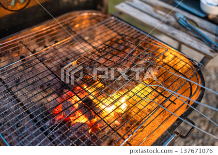 Barbecue grill with meat and burning fire on BBQ grill in backyard Barbecue grill with meat and burning fire on BBQ grill in backyard 137671076