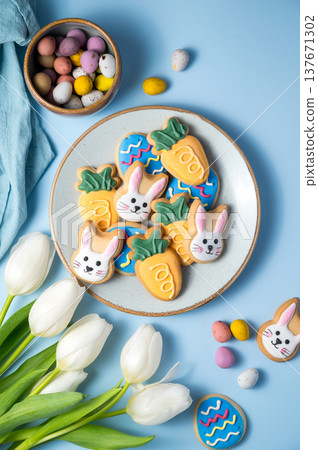 Easter spring holiday background with easter cookies in a plate: bunny, carrot and egg with white tulips Easter spring holiday background with easter cookies in a plate: bunny, carrot and egg with white tulips 137671302