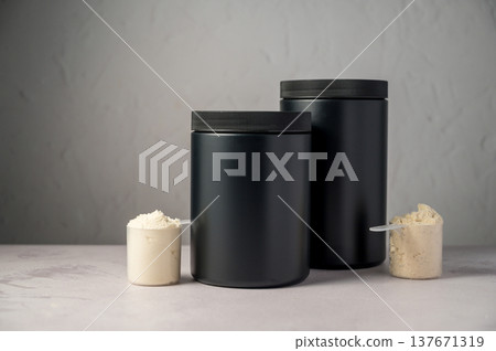 Protein powder in scoops with black protein tubes, jars in background. Body building, muscle growth and food supplement concept 137671319