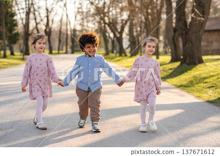 Diverse children holding hands walking together in a park Diverse children holding hands walking together in a park 137671612