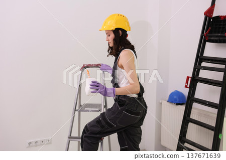 Creative woman painting indoors with ladders and tools in a bright room full of potential Creative woman painting indoors with ladders and tools in a bright room full of potential 137671639