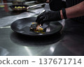 Professional chef plating a piece of fried fish on a black ceramic plate in a restaurant 137671714