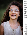 Close up portrait of a laughing little girl with curly hair wearing stylish golden glasses outdoors 137671727