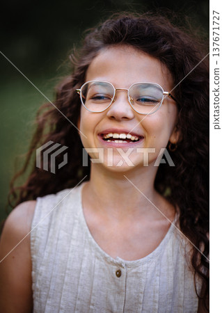 Close up portrait of a laughing little girl with curly hair wearing stylish golden glasses outdoors 137671727