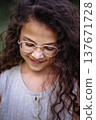 Close up portrait of a smiling young girl with long curly hair and glasses looking down 137671728
