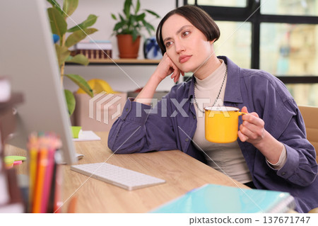 Contemplating thoughts over coffee while working at a cozy desk in a bright and inviting office space 137671747