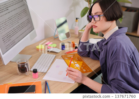 Creative focus in a serene workspace as a young woman sketches and plans her artistic projects surrounded by colors and inspiration 137671760
