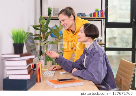 Two friends collaborate on a creative project in a bright study filled with plants and vibrant colors during a sunny afternoon 137671763