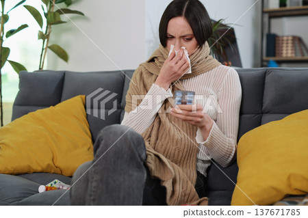 Woman in a cozy living room dealing with a cold while wrapped in a blanket, surrounded by comfort 137671785
