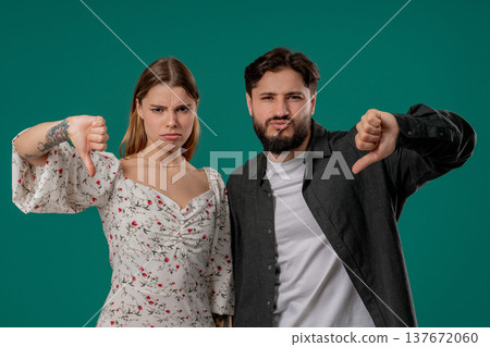 Young Couple Giving Thumbs Down Dislike With Disapproving Look On Green Backdrop Young Couple Giving Thumbs Down Dislike With Disapproving Look On Green Backdrop 137672060