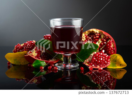 Pomegranate and a glass of ruby-red juice on a black reflective background. Pomegranate and a glass of ruby-red juice on a black reflective background. 137672713