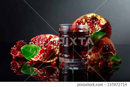 Pomegranate and a glass of ruby-red juice on a black reflective background. Pomegranate and a glass of ruby-red juice on a black reflective background. 137672714