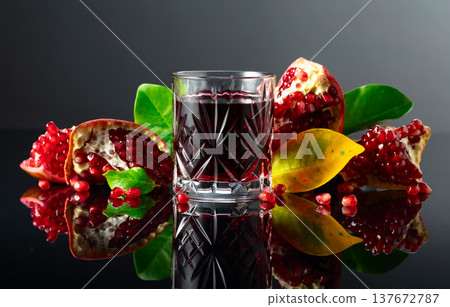 Pomegranate and a glass of ruby-red juice on a black reflective background. 137672787
