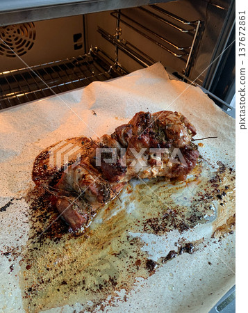 Turkey meat is placed in the oven on a baking tray lined with paper. The tray has grease and cooking residue from the turkey. Herbs are visible on the meat Turkey meat is placed in the oven on a baking tray lined with paper. The tray has grease and cooking residue from the turkey. Herbs are visible on the meat 137672861