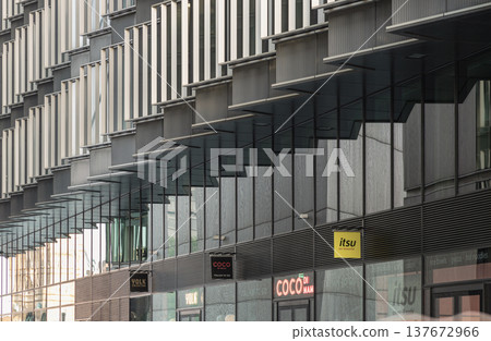 The large glass surfaces of the building ground floor act as mirrors, capturing and repeating the complex, rhythmic patterns of the overhead architectural fins to create a stunning, layered visual The large glass surfaces of the building ground floor act as mirrors, capturing and repeating the complex, rhythmic patterns of the overhead architectural fins to create a stunning, layered visual 137672966