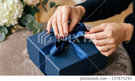 Manicured Hands Untying Silk Ribbon on Premium Gift Box 137673293