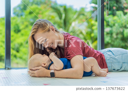 Mother and baby lying on a soft play mat at home, playing, talking and sharing a joyful moment together. Authentic family lifestyle, early childhood development and emotional bonding. Parenting and 137673622