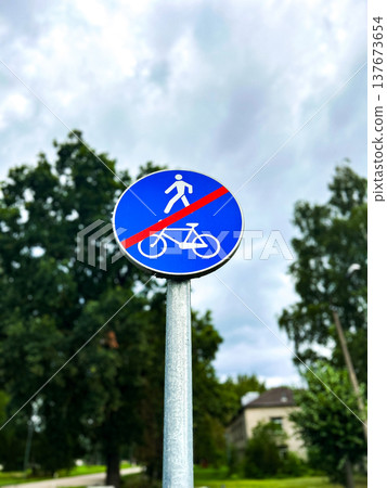 End of pedestrian and bicycle path. Round blue road sign crossed with red line. Urban settings against green trees and blue sky. Vertical photo End of pedestrian and bicycle path. Round blue road sign crossed with red line. Urban settings against green trees and blue sky. Vertical photo 137673654