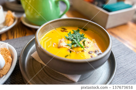 Pumpkin soup served on table. Pumpkin cream soup with seeds and greens. Cozy atmosphere. 137673658