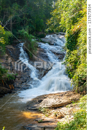 Mae Sa waterfalls near Chiang Mai Thailand surrounded by lush green jungle. Flowing water and tropical forest create serene nature scene, ideal for travel, adventure and eco-tourism concepts. Mae Sa waterfalls near Chiang Mai Thailand surrounded by lush green jungle. Flowing water and tropical forest create serene nature scene, ideal for travel, adventure and eco-tourism concepts. 137673934