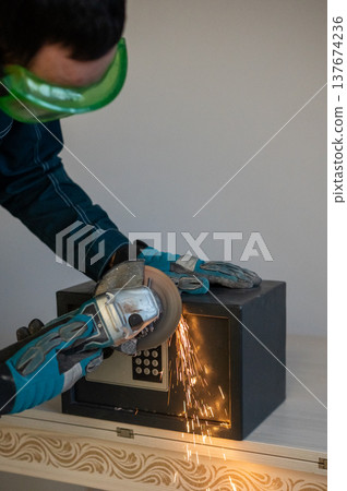 A man breaks into a safe with a grinder. 137674236
