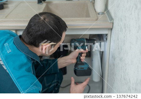 The technician removes the door from the kitchen cabinet. The technician removes the door from the kitchen cabinet. 137674242