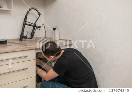 A plumber is replacing a faucet in the kitchen. A plumber is replacing a faucet in the kitchen. 137674249