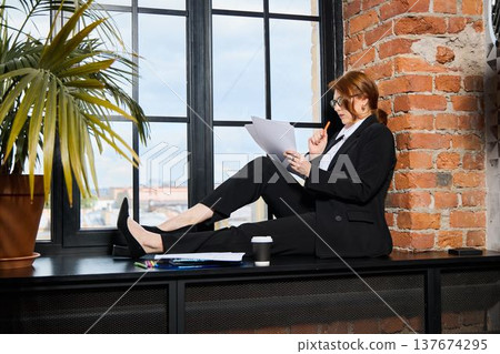 Project manager reviewing files at windowsill Project manager reviewing files at windowsill 137674295