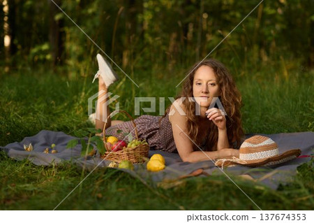Woman of pale complexion sitting peacefully among grass with fruit basket Woman of pale complexion sitting peacefully among grass with fruit basket 137674353