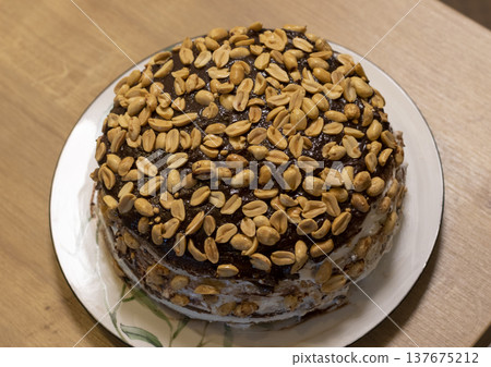 A multi layered cake covered in chocolate icing and topped with a large amount of roasted peanuts 137675212