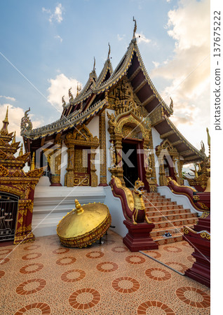 Exterior of Wat Rajamontean in Chiang Mai at sunset with golden temple entrance, naga stair guardians and dramatic sky. Historic Lanna style site offering cultural travel appeal. 137675222